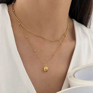 Double-layered golden necklace with bead chains and minimalist water drop pendant