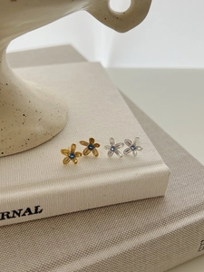 Détail macro de boucles d'oreilles fleurs en argent et or avec pierres bleues et métal brossé