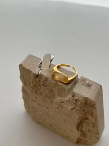 Macro shot of minimalist gold and silver rings with oval chalcedony on stone surface