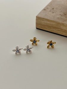 Détail de boucles d'oreilles fleur mat avec pierres bleues sur support en pierre