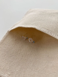 Detail of gold oval pink crystal earrings with blue stone accent on linen pouch