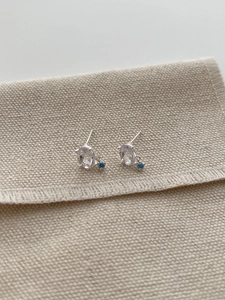Detail of 925 silver stud earrings with blue topaz stones on a beige canvas pouch