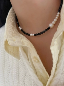 Detail of 925 black onyx and gradient pearl necklace worn on neck with white clothing