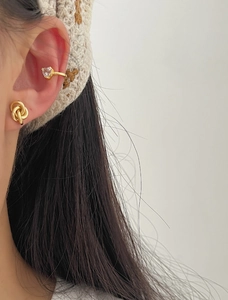 Detail of gold knot stud and heart gemstone ear cuff set on model with soft lighting