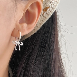 Minimalist 925 sterling silver bow charm hoop earrings worn on a model's ear