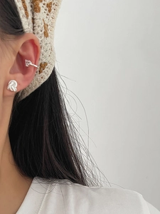 Detailed view of silver knot stud and heart crystal ear cuff on a model's ear