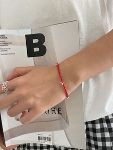 Detail of red beaded bracelet and silver flower ring styled on hand with a magazine