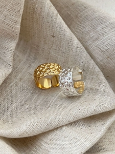 Detailed view of wide textured open rings in gold and silver finish on linen fabric