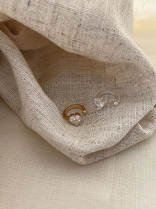 Close-up of gold and silver heart-shaped zircon ear cuffs on beige linen fabric