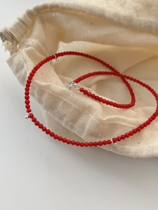 Détail de collier en perles rouges avec billes en argent sur pochon en lin