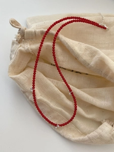 Détail macro d'un collier de perles corail rouge et argent S925 sur une pochette en lin