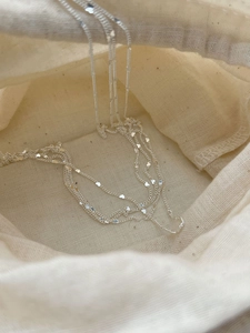Macro view of minimalist 925 silver layered necklace with tiny heart sequins on linen