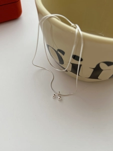 Detailed macro of a silver cherry bead pendant necklace hanging on a ceramic cup
