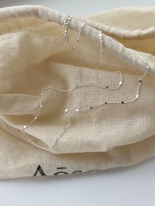 Detail of silver heart charm necklace resting on minimalist linen fabric bag