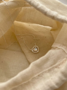 Detailed close-up of a silver heart necklace with moonstone on a linen gift bag
