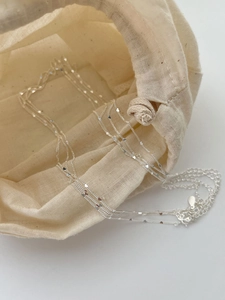 Detail of layered 925 silver necklace with heart sequins and linen drawstring bag