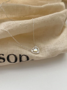 Detail of S925 sterling silver heart pendant with moonstone on textured linen