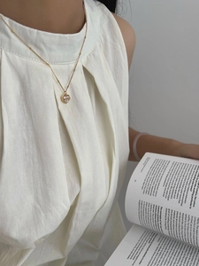 Détail du collier pendentif cœur avec ruban doré sur modèle lisant un livre