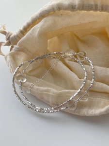 Detail of silver beaded necklace with crystal butterfly heart charm on linen pouch