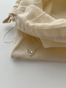 Close-up of S925 silver heart necklace with moonstone on a rustic burlap gift pouch