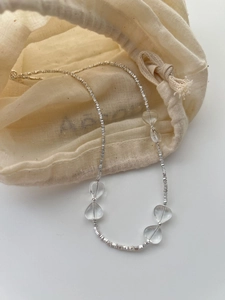 Detail of silver beaded necklace with transparent heart charms on linen pouch