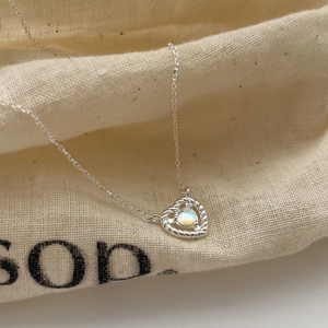 S925 silver heart necklace with moonstone on a textured beige fabric pouch background