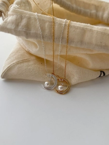 Detail of moon pendant with pearl and zircon inlay hanging on a beige linen bag