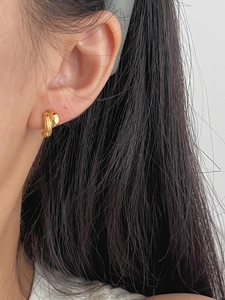 Close-up of elegant gold stud earrings with textured wavy design on ear lobe