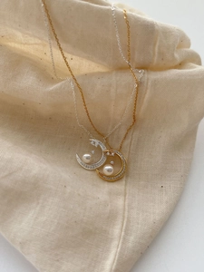 Close-up of crescent moon necklace with zircons and pearl on natural beige linen background