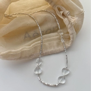 Handmade silver beaded necklace with clear heart charms on a beige linen jewelry pouch