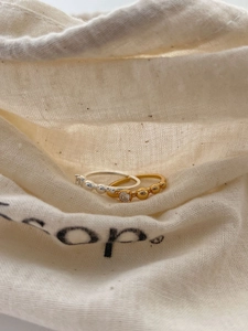 Detail of silver bead ring and gold zircon ring on a soft cream linen pouch background
