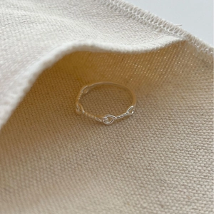 Minimalist 925 sterling silver twisted knot ring on a beige canvas pouch background