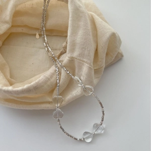 Minimalist silver beaded necklace with heart-shaped glass charms on a linen pouch
