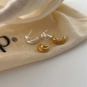 Minimalist curved metal stud earrings in gold and silver finish on a fabric bag