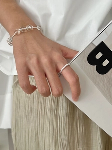Close-up of a s925 silver twist ring and a clear beaded bracelet worn by a model