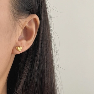 Elegant gold heart stud earring with textured bow engraving worn on model ear