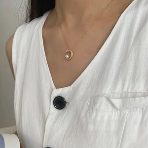 Elegant gold necklace with crescent moon pearl pendant worn by model on white linen