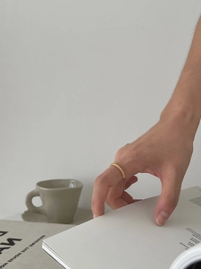 Detail of a thin gold twisted rope ring worn on the finger in a minimalist setting