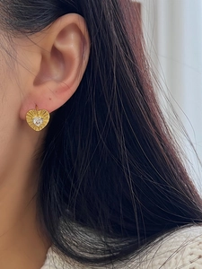 Detail of gold heart earrings with zircon inlay and sunburst texture worn by a model