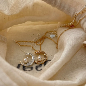 Elegant crescent moon pearl necklace in silver and gold tones on a linen jewelry pouch