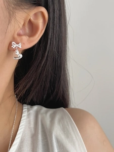 Détail de boucles d'oreilles nœud et cœur en argent S925 portées par un mannequin femme