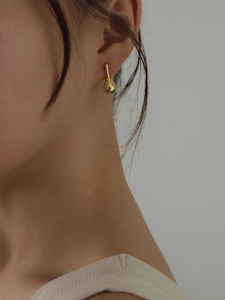 Close-up of a minimalist gold teardrop earring with polished finish worn by a model