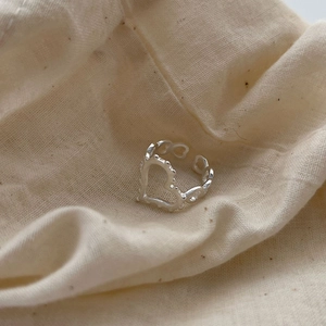 Bague ouverte en argent 925 à motif cœur géométrique sur fond lin beige