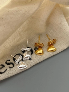 Détail de boucles d'oreilles nœud cœur en argent et or sur tissu de lin beige