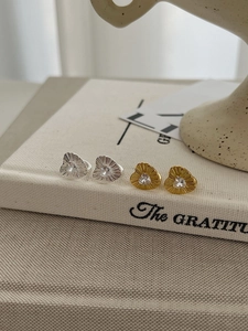 Close-up of heart-shaped gold and silver earrings with zircon stones and radial texture