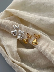 Détail de boucles d'oreilles nœud et cœur en argent et or avec bordure torsadée
