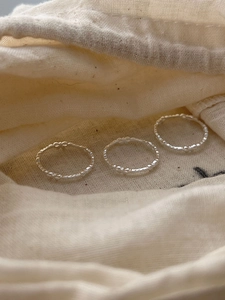 Detailed view of three minimalist 925 sterling silver bow rings on a soft beige fabric pouch