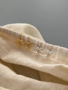 Detail of silver and gold knot drop earrings hanging on a textured beige linen bag
