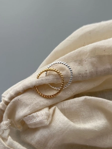 Close-up of gold and silver beaded twist rings on a soft beige linen texture pouch