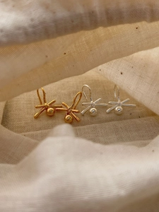 Detail of 925 silver and gold lucky knot drop earrings on soft linen fabric texture